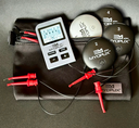 An image of the MyoPux eDN device which includes a wireless controller, wires with Pomona clips, and multiple Pux units in black and white colors.